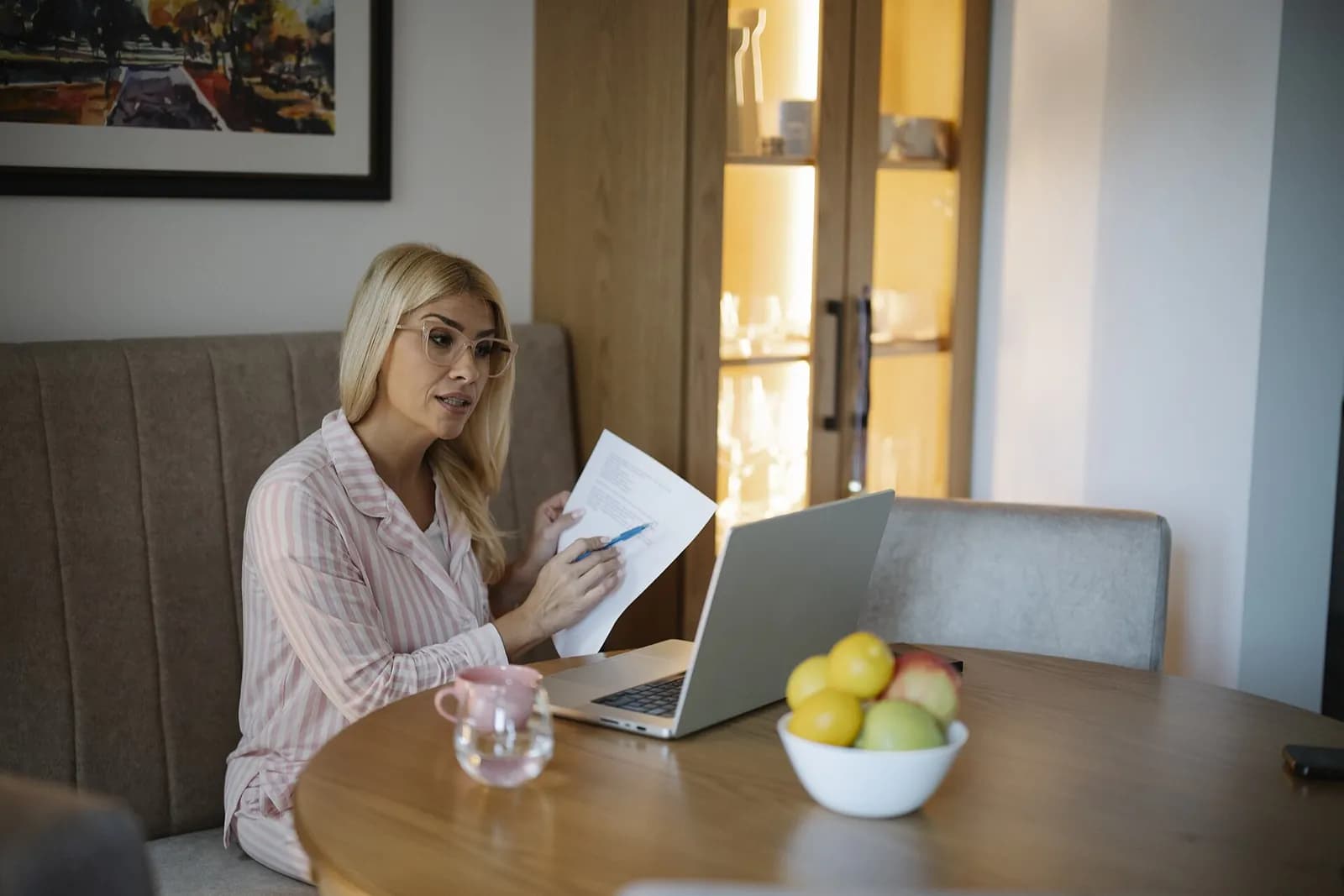 Woman at a table with a laptop reviewing a printed document