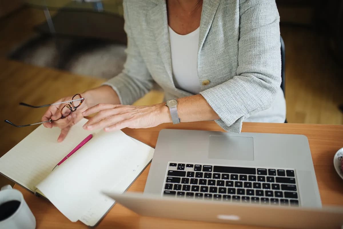 Hands turning the pages of a notebook next to a laptop on a desk