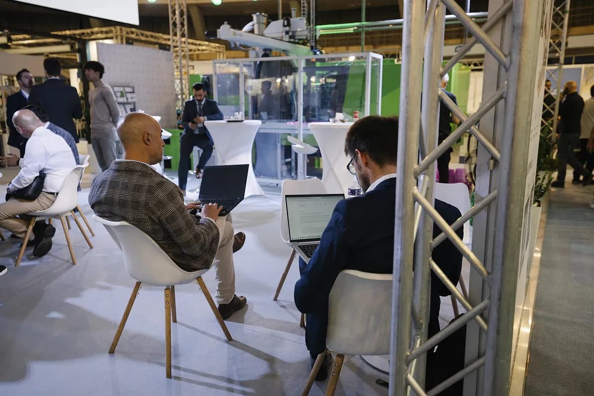 Professionals working on laptops at a conference event with other attendees in the background