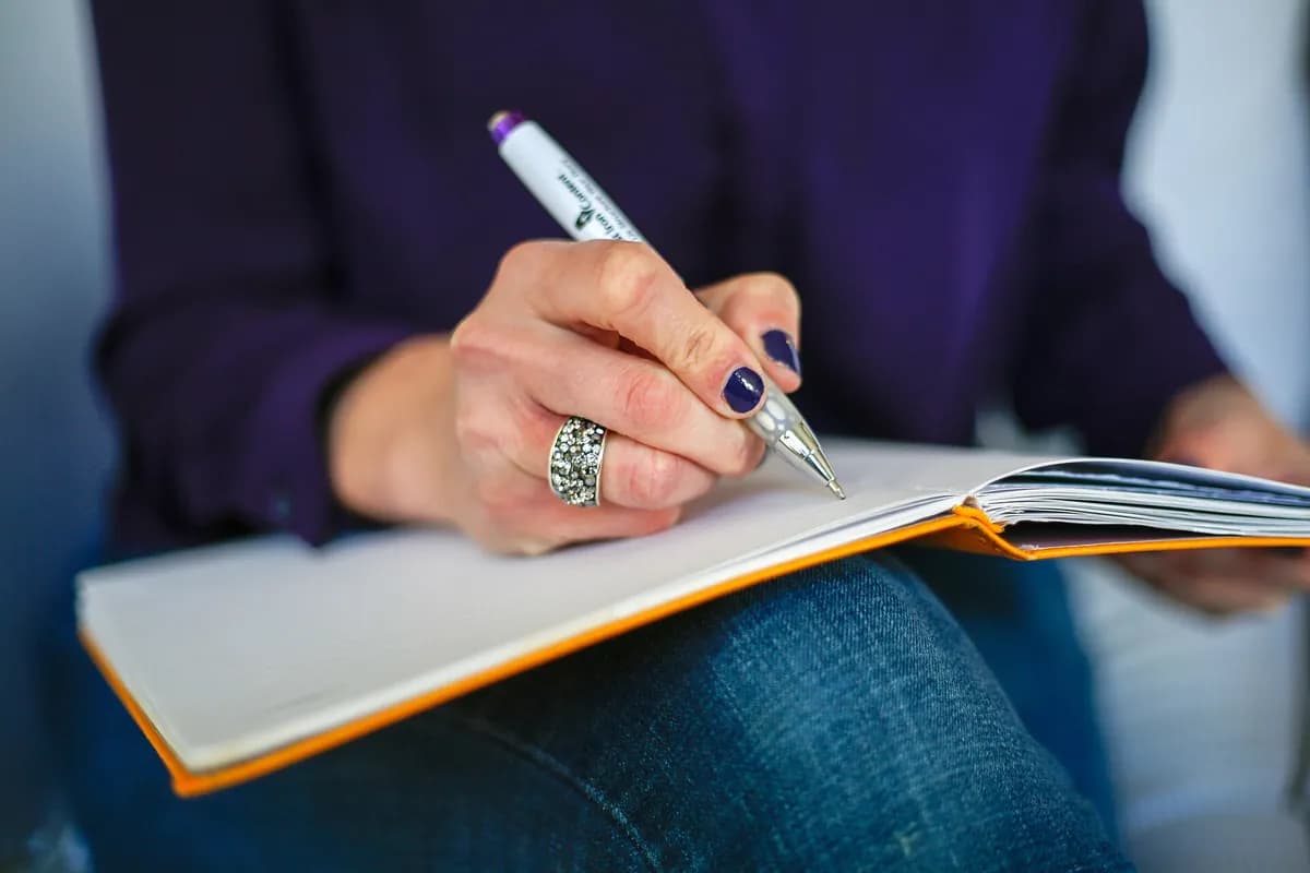Woman writing notes in an orange notebook with a pen