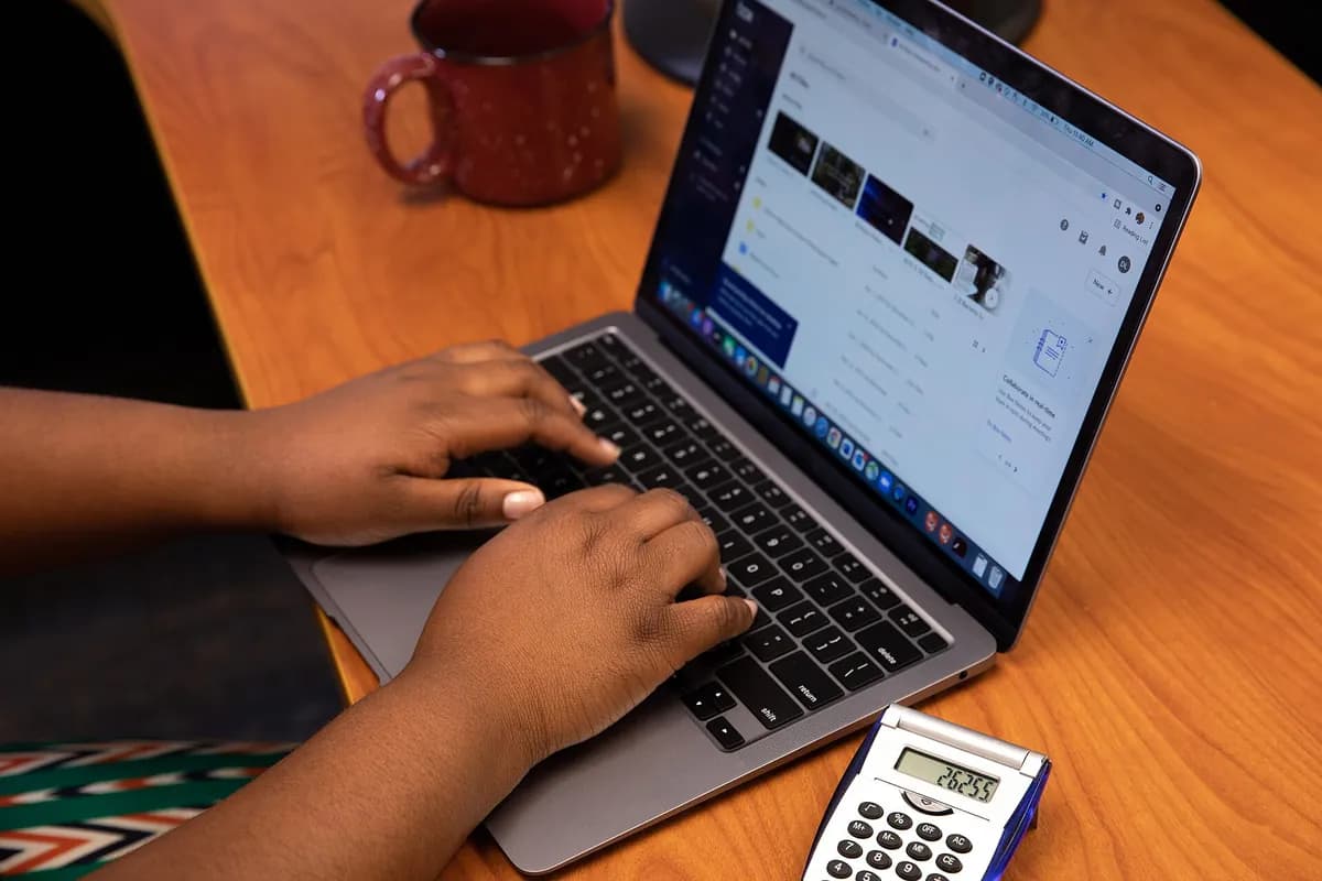 Hands typing on a laptop next to a calculator and a coffee mug